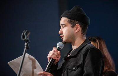 a student in a hat holding a microphone and speaking.