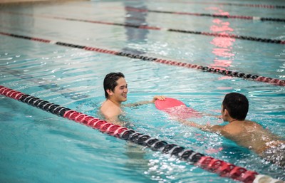 Two students in the pool. One is being pulled on a kick board by the other.