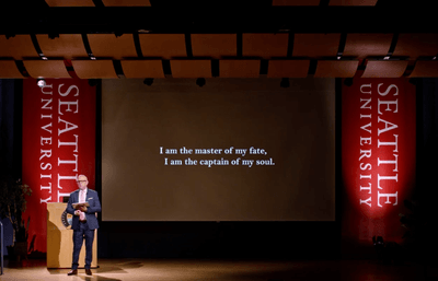 Provost on stage in front of slide presentation