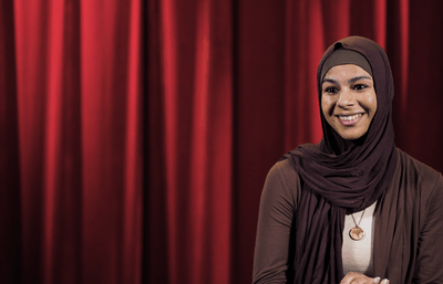 Seattle University student Imaan smiling in front of red curtain backdrop.