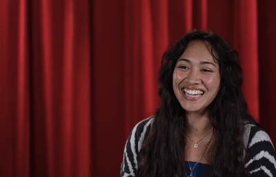 Seattle University student Sofia smiling in front of red curtain backdrop.
