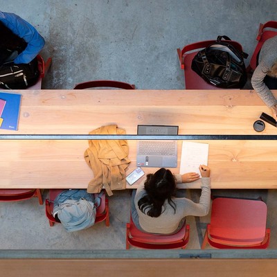 A photo from above looking down on three students studying at a long wooded table.