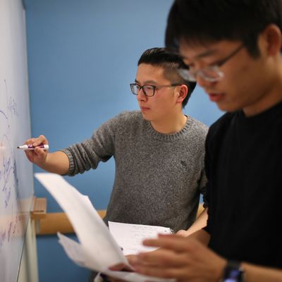 Graduate student Bowen Chen (MSF), from Shanghai China, center, writes out a finance problem in the library on campus in preparation for his final.