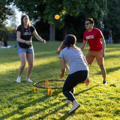 Three students playing roundnet on a green grassy lawn in the summer