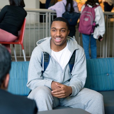 Smiling student sitting on a blue chair in conversation with another