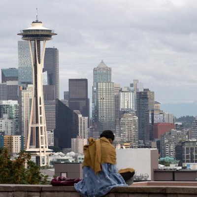 A woman sits on a ledge overlooking the seattle skyline.