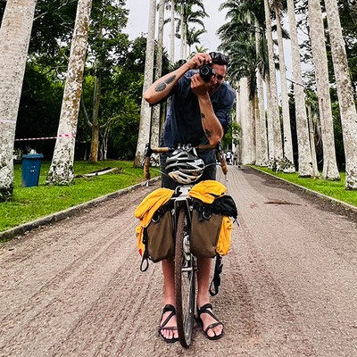 Man on bike on gravel road holding camera to his face