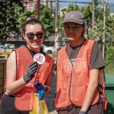 Two volunteers wearing orange safety vests and gloves smile while participating in 91̽��'s Alumni Day of Service.
