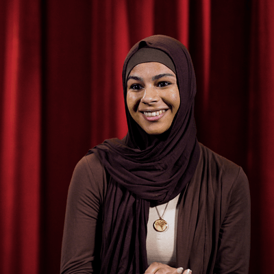 Seattle University student Imaan smiling in front of red curtain backdrop.