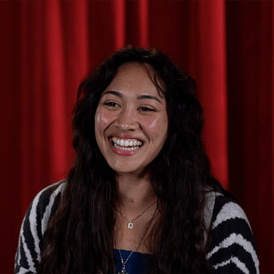 Seattle University student Sofia smiling in front of red curtain backdrop.