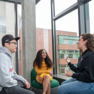 Three graduate students talk inside the Sinegal building