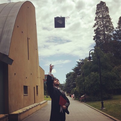 A graduate tossing a mortarboard in the air on the lower mall of campus