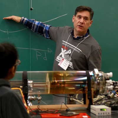A man in front of a blackboard pointing to a machine.