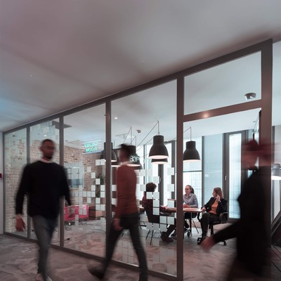 A busy office with workers walking past an occupied meeting room.