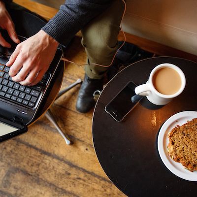 Hand typing on a laptop next to their coffee, pastry, and phone
