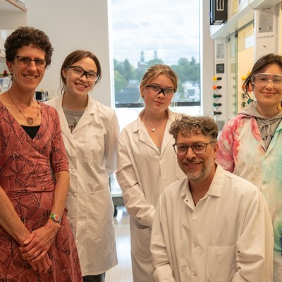 Group of students and faculty in lab coats smiling for the camera.