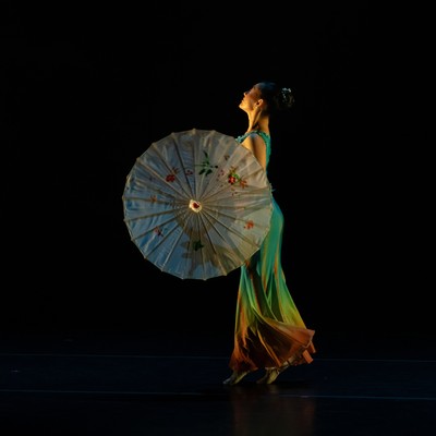 a dancer on stage in costume with paper parasol