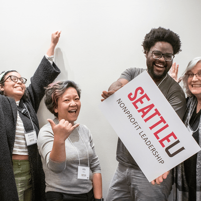 Four alumni with a sign showing the logo