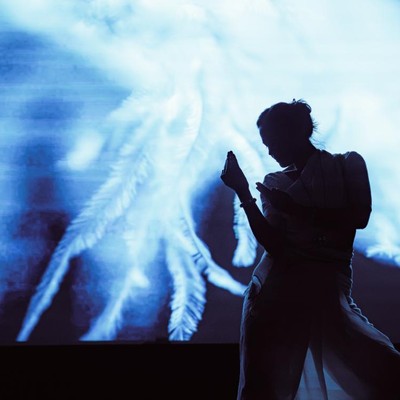 Still of Doshi mid performance with background screen.