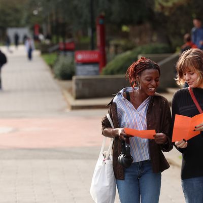Two students speaking while looking at flyers and walking through campus