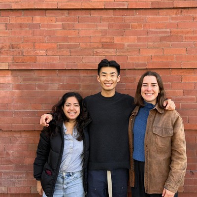 three Students posing in front of a red brick wall