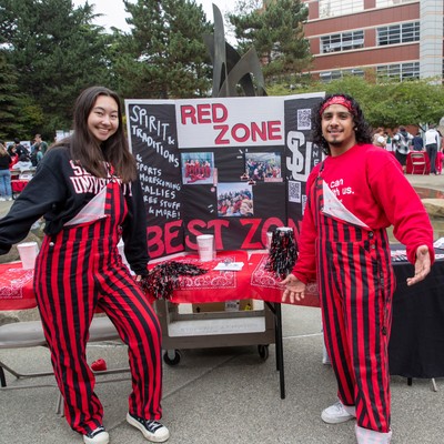 Two students with wide open standing in front of a Red Zone table at the Fall Involvement Fair