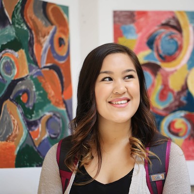 A student standing in front of two colorful paintings