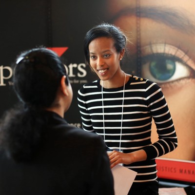 A woman in a striped shirt talking to a student with her back turned.