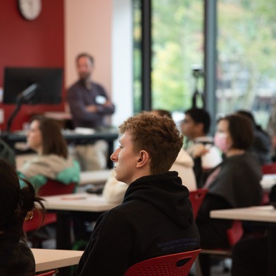 People sitting in a modern glass-walled classroom listening to a presentation