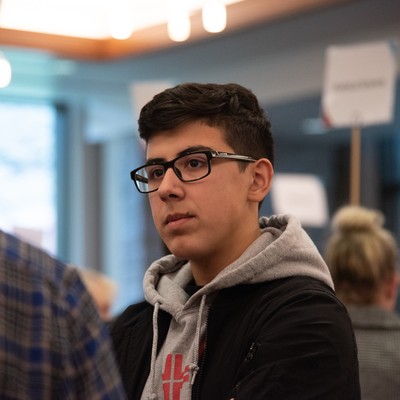 A student wearing glasses in conversation with another person.