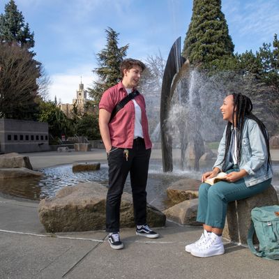 Two students talk by a fountain on campus