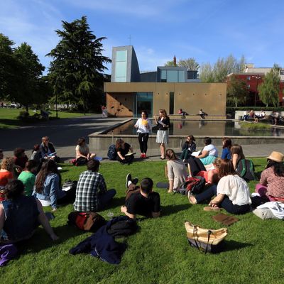 Class sits on green grass in front of chapel while professor talks