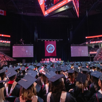 A large crowd of graduates in caps and gowns in a stadium.