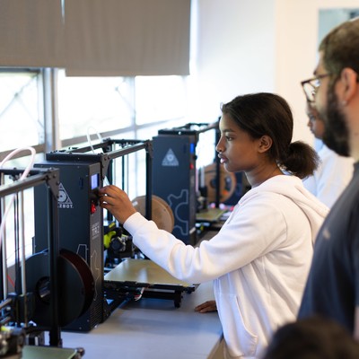 A group of people looking at a 3d printer.