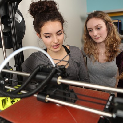 Three students look at a 3d printer.
