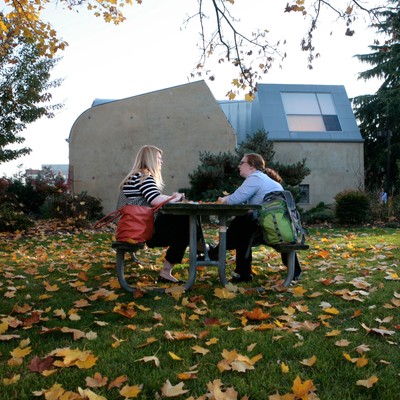 Two persons having a conversation in a outside table in the campus surrounded by fall colors