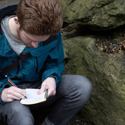 A man sitting on a rock writing on a plate.