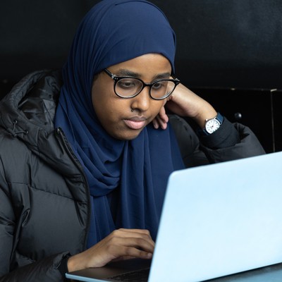 A woman wearing glasses and a blue scarf looking at a laptop.