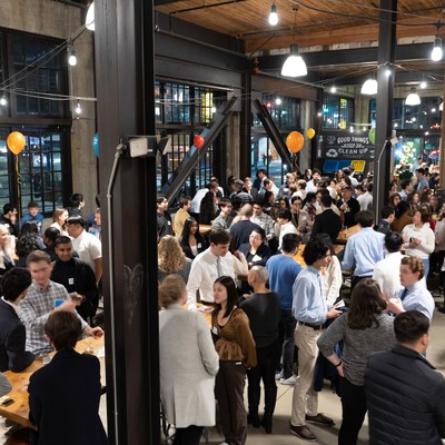 Crowd of people engaged in conversations at an indoor event with balloons and string lights.