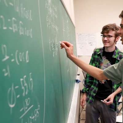 People solving problems on a blackboard in a classroom