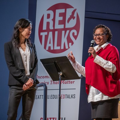 Two women standing in front of a red talks sign.