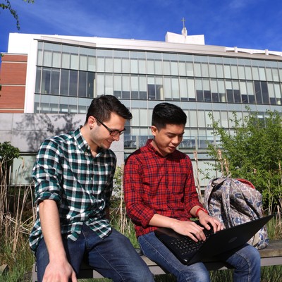 Two students sitting on a bench in front of a building.