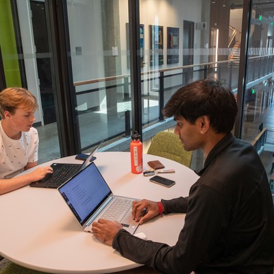 Two people sitting at a table with laptops.
