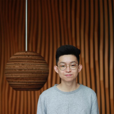 A student standing beside a wooden hanging lamp.
