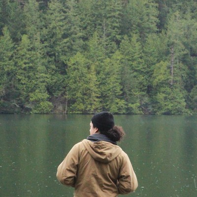 A student looks out over a lake surrounded by evergreen trees in a reflective moment on Outdoor Retreat.