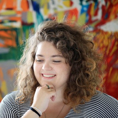 A curly headed student smiling against the backdrop of a modern painting
