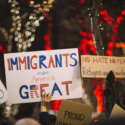 Image of cardstock banners on a protest at night time. The main banner says 'immigrants make America Great'