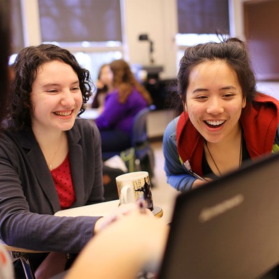 A trio of students conferring and laughing over a laptop.