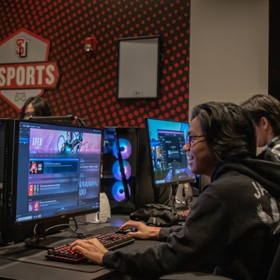 A group of people sitting at desks in a gaming room.