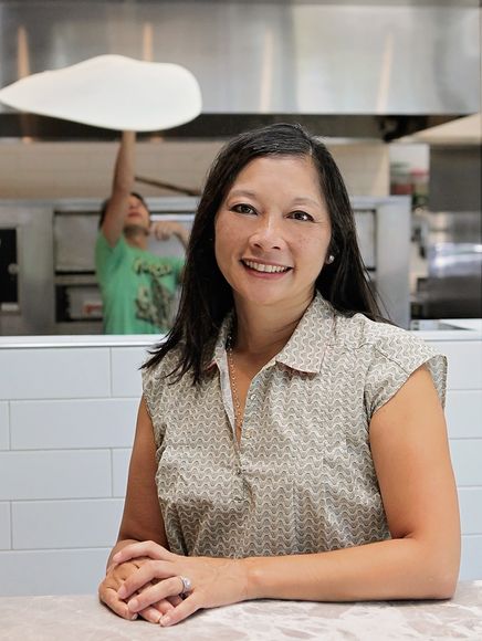 Pagliacci co-owner Michelle Galvin in the foreground with her son tossing a pizza in the background